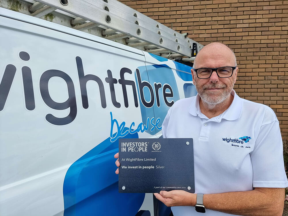 John Irvine stands next to a WightFibre van holding an Investors in People Silver award plaque.