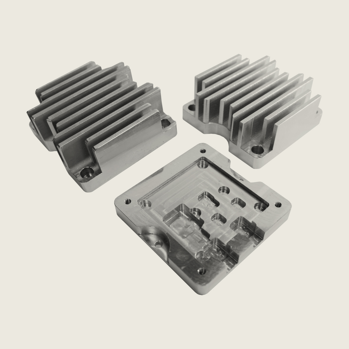Three shiny metal heat sinks with fins and mounting holes on a plain background.