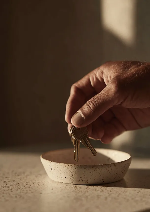 A hand placing a set of keys into a small ceramic bowl.