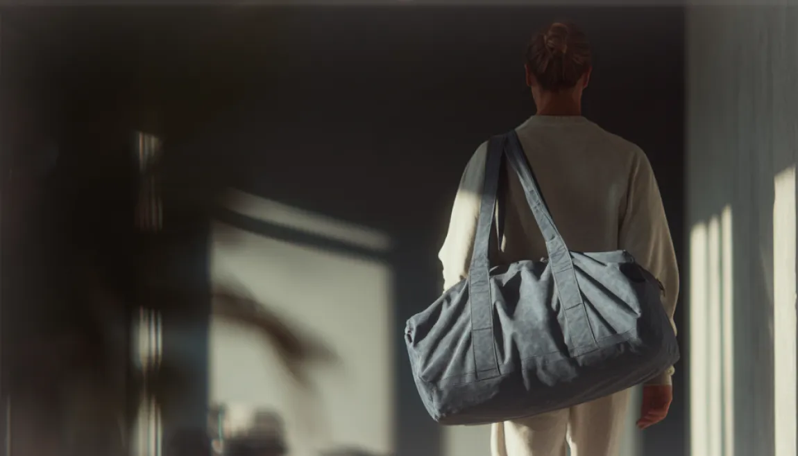 A person walking down a hallway carrying a large duffel bag.