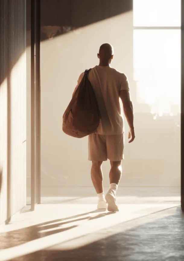 Person walking into a sunlit interior carrying a gym bag