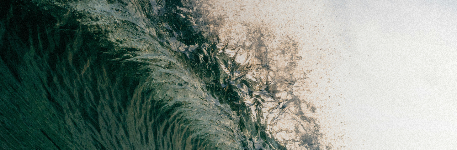 Ola de agua azul oscura formando espuma hacia la derecha con fondo claro.