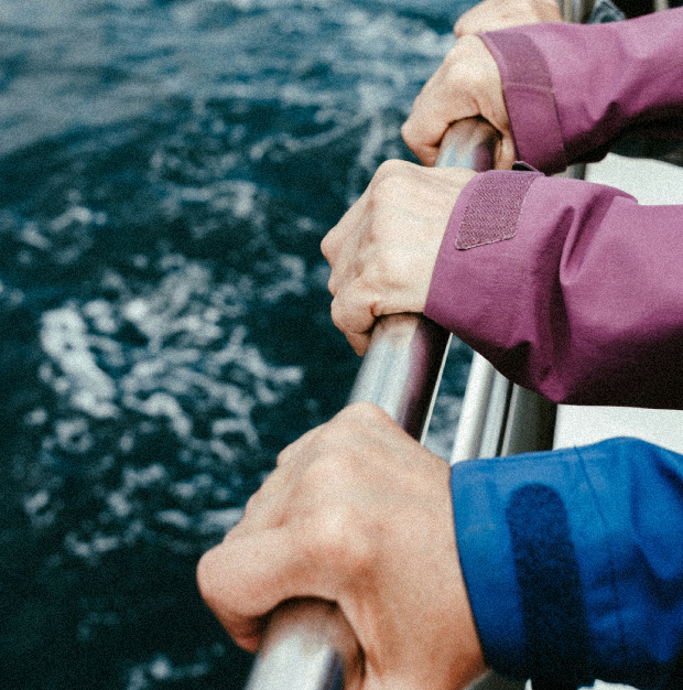 Dos personas sujetando la barandilla metálica de un barco mientras navega en el agua.