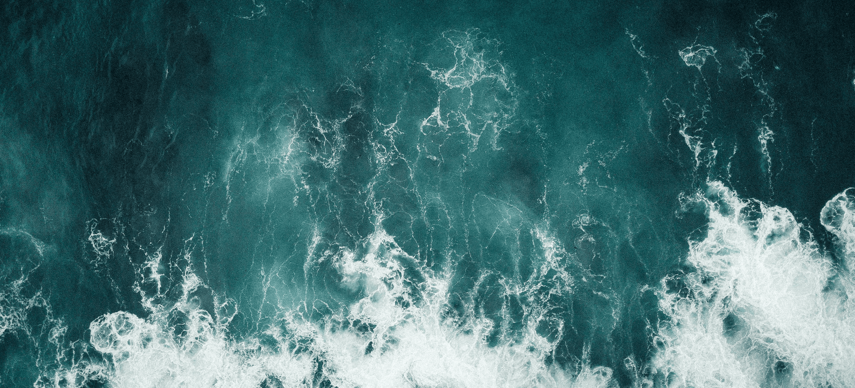 Vista aérea de olas blancas rompiendo sobre agua oceánica azul oscura.