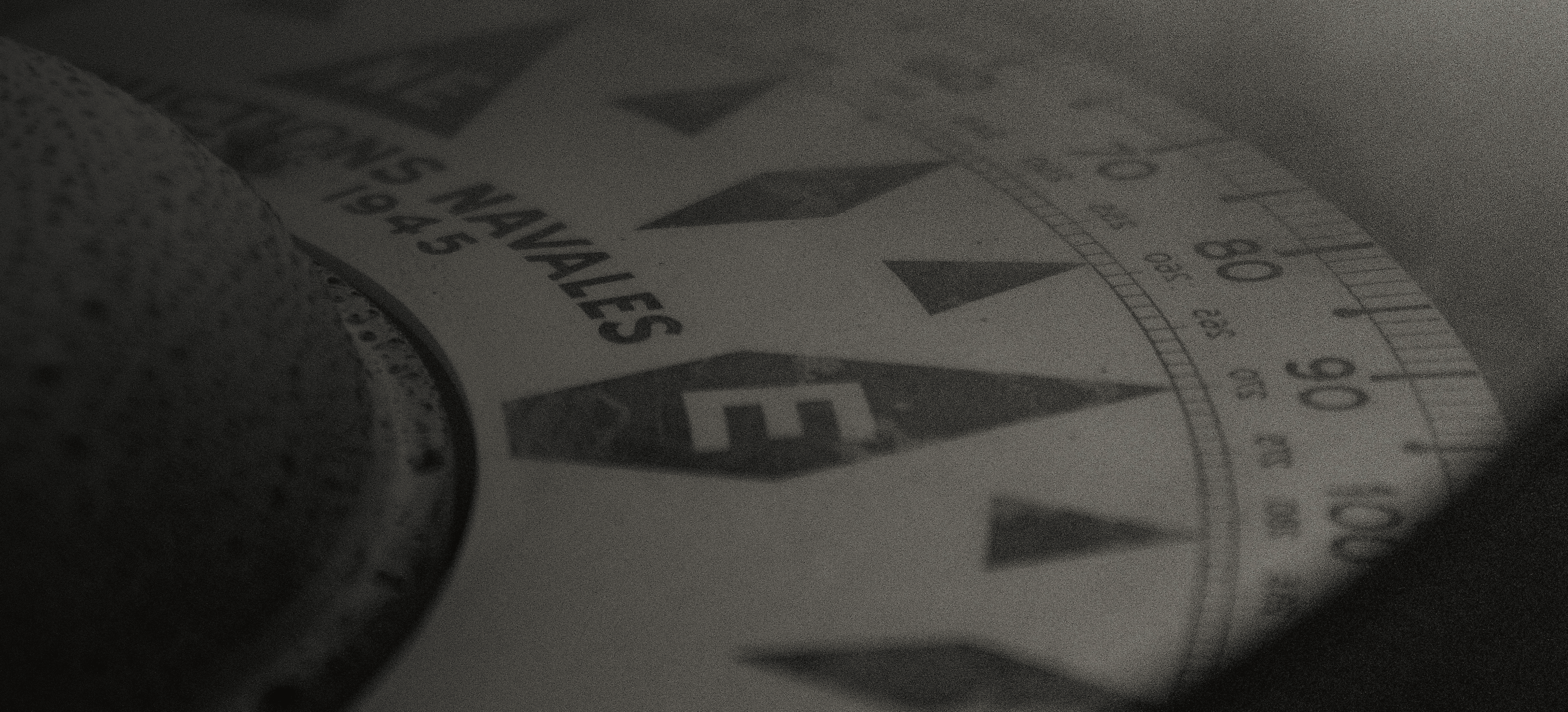 Primer plano de una brújula de estilo antiguo mostrando dirección este y texto ‘U.S. NAVALS 1945’.