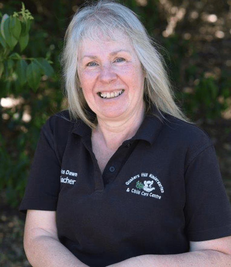 Miss Dawn wearing a black polo shirt embroidered with Quakers Hill Kindergarten & Child Care Centre logo and the name Chris Dawn Teacher.
