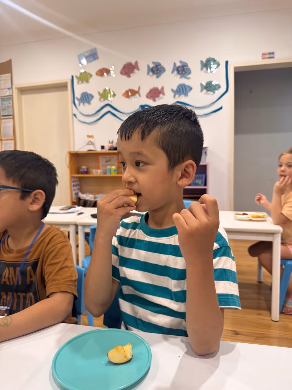 Young boy in a red spider web shirt focused on assembling colorful plastic gears at a table in a classroom. A student from Quakers Hill Kindergarten & Child Care Centre. 