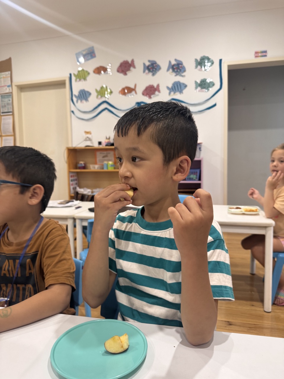 Young boy in a red spider web shirt focused on assembling colorful plastic gears at a table in a classroom. A student from Quakers Hill Kindergarten & Child Care Centre. 
