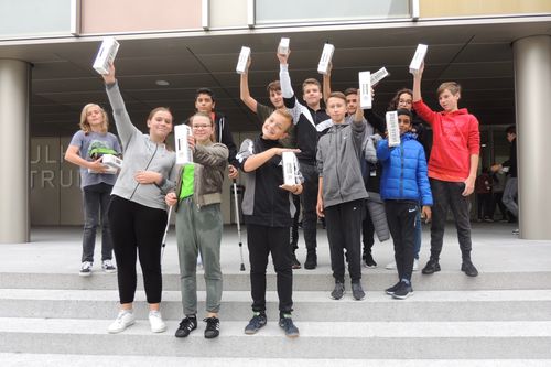 Group of smiling teenagers standing on concrete steps holding steel bottle boxes, posing outdoors in front of a building and celebrating tap water.