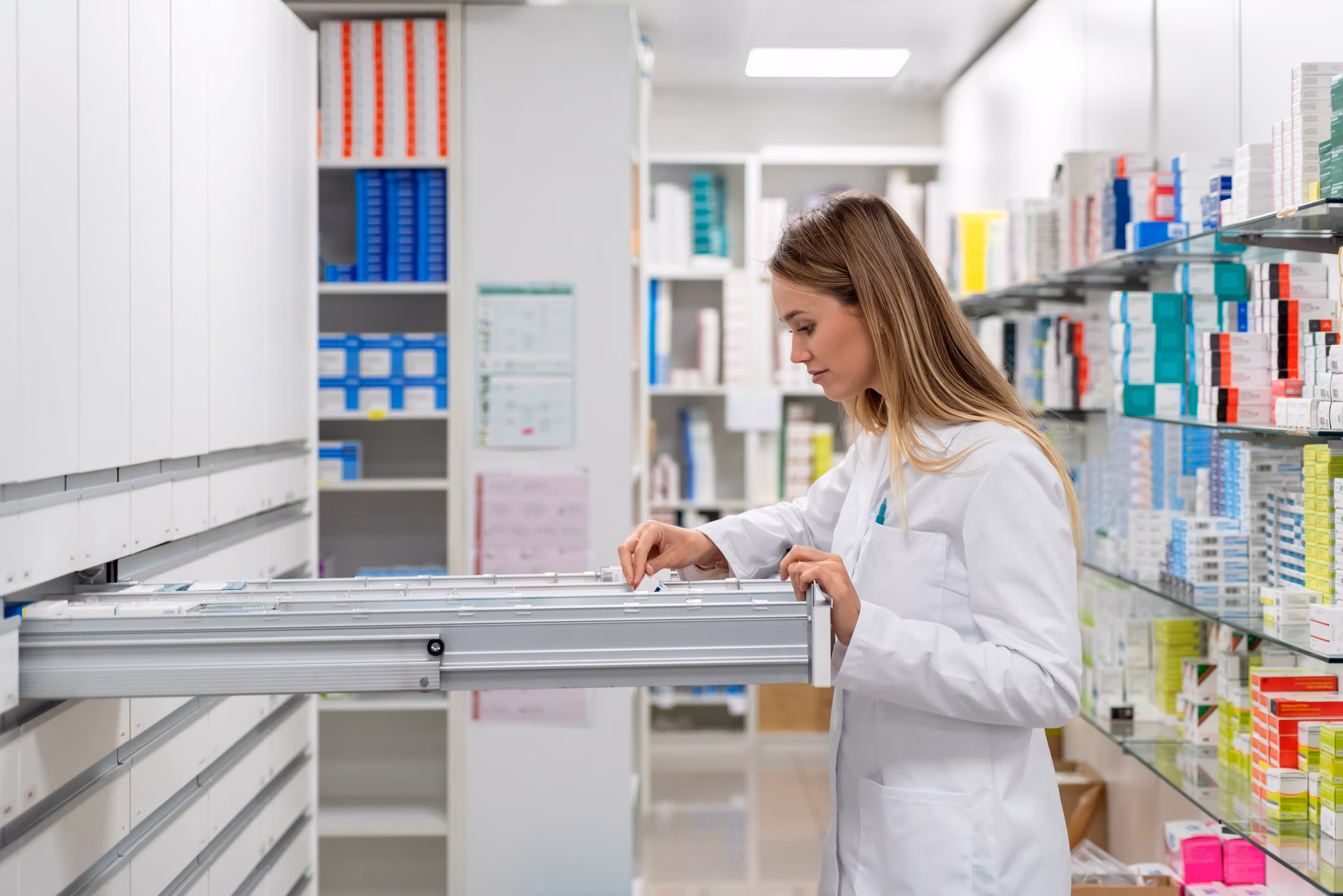 Apotheker in wit labjas die medicatie uit een lade in de apotheek bekijkt.