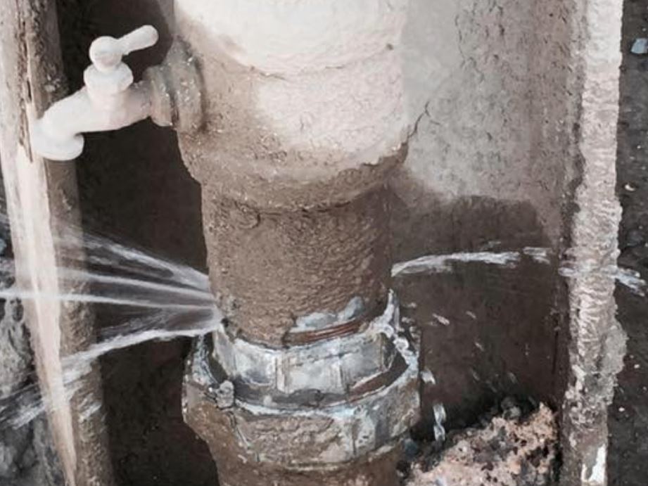 Close-up of a damaged copper pipe with a visible crack and water leaking from the joint.