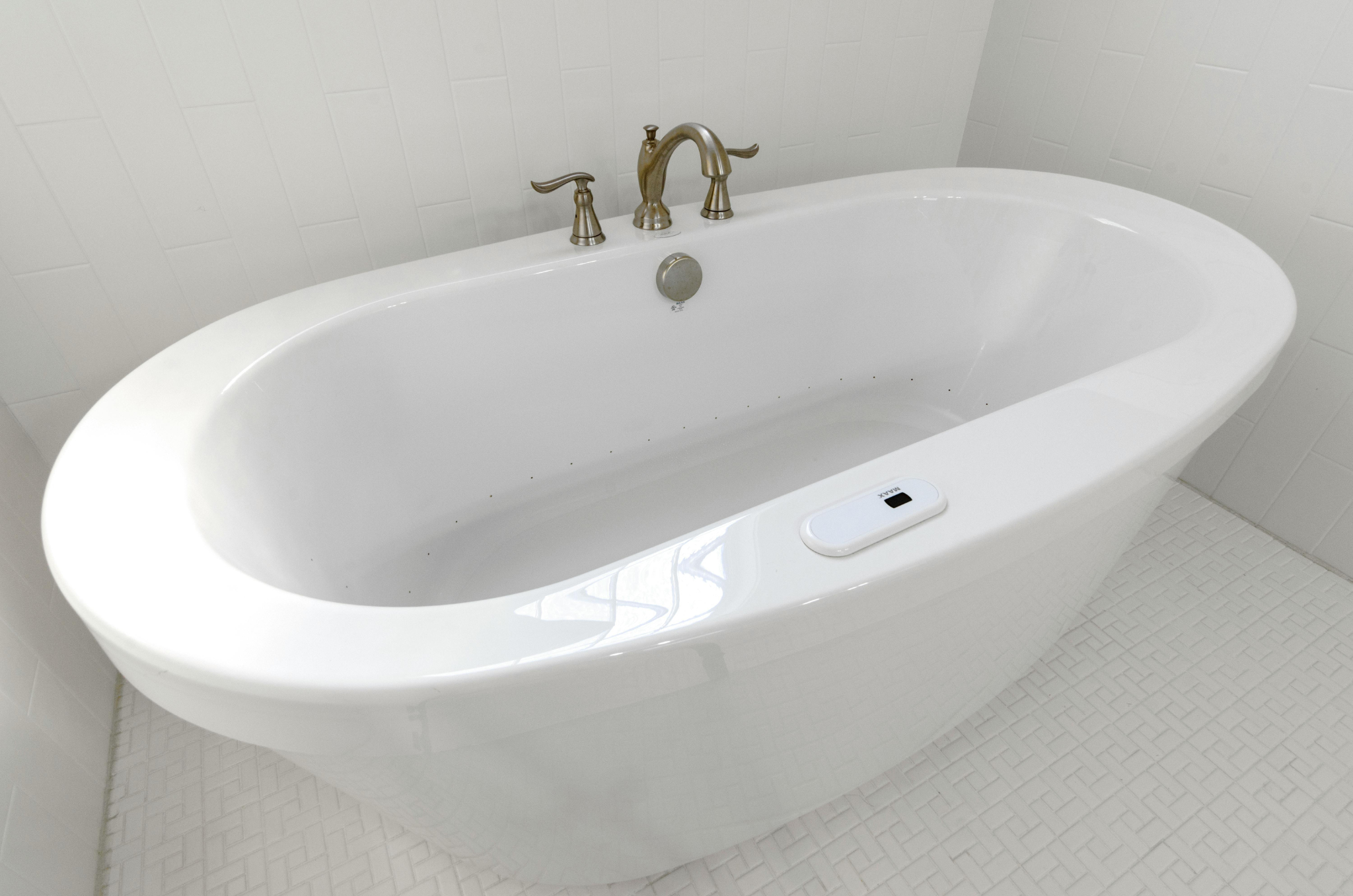 White freestanding bathtub with silver faucet and control panel in a tiled bathroom.