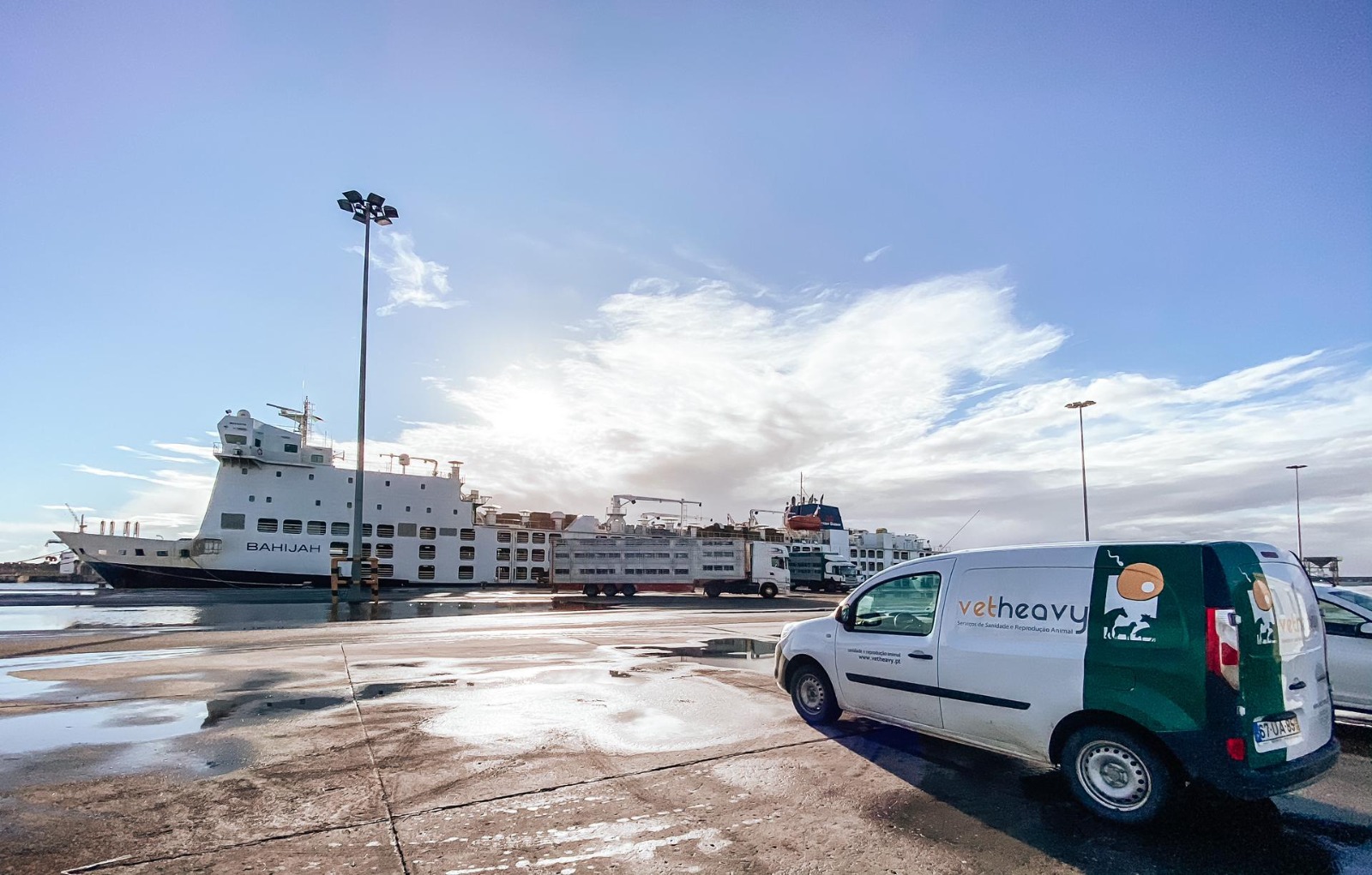 Carrinha vetheavy estacionada perto de um porto com um grande navio chamado BAHIJA no fundo.