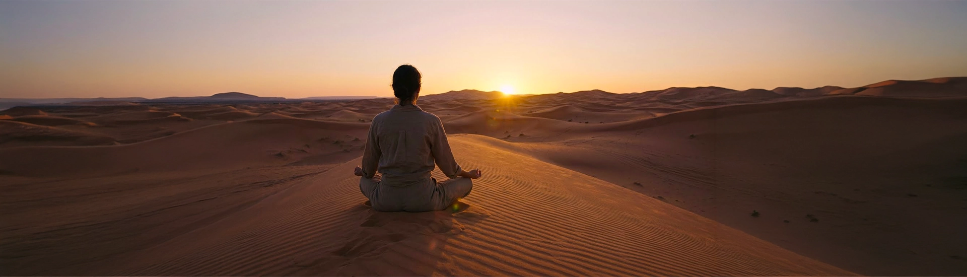 A traveller meditating among the dunes of Erg Chebbi at sunset.