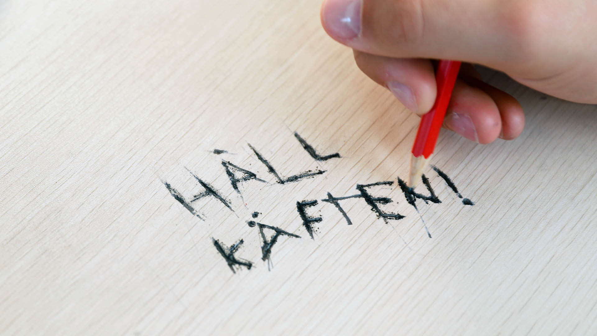 Närbild på en hand inne i en buss där ett finger precis ska trycka på en stoppknapp. Knappen är gul med en röd mittpunkt och är monterad på den mörka listen under ett fönster. 