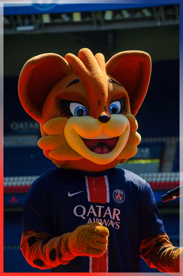 PSG sports mascot with big blue eyes and orange fur wearing a navy blue Qatar Airways jersey on a soccer field.