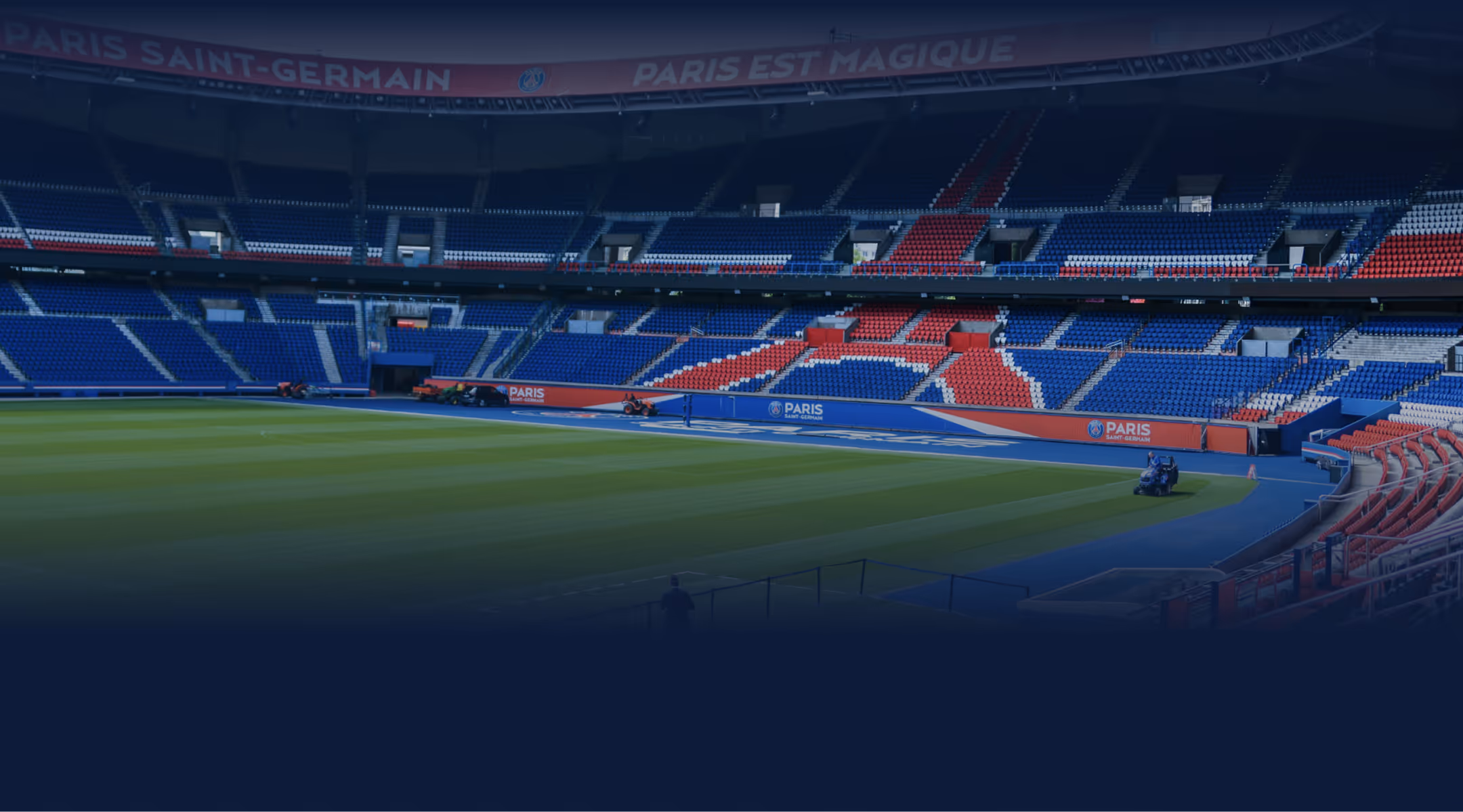 Empty Paris Saint-Germain soccer stadium with green field and seating in blue, red, and white colors.