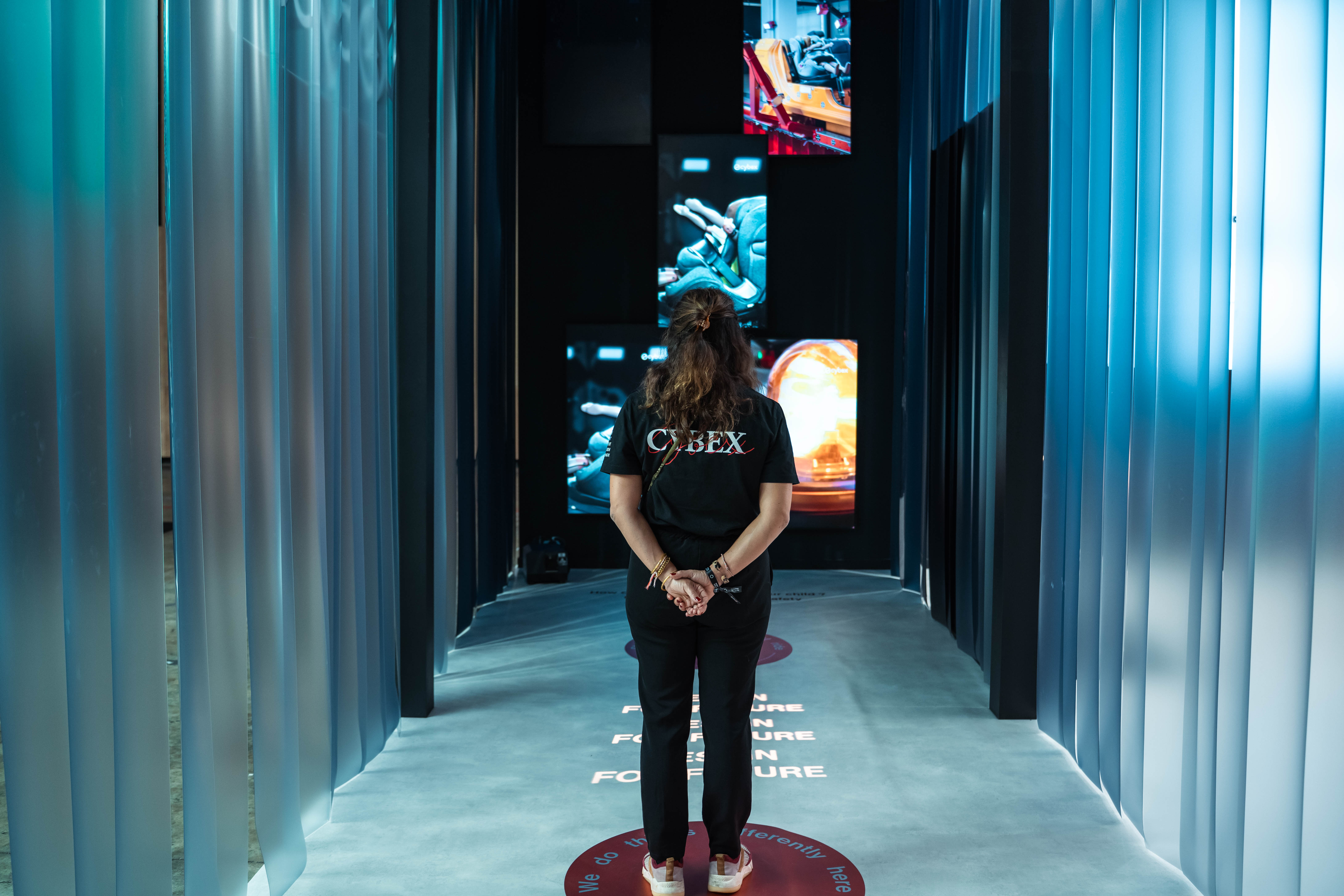 Tunnel immersif du stand Cybex : lanières de bâche cristal, textes projetés au sol et écrans
