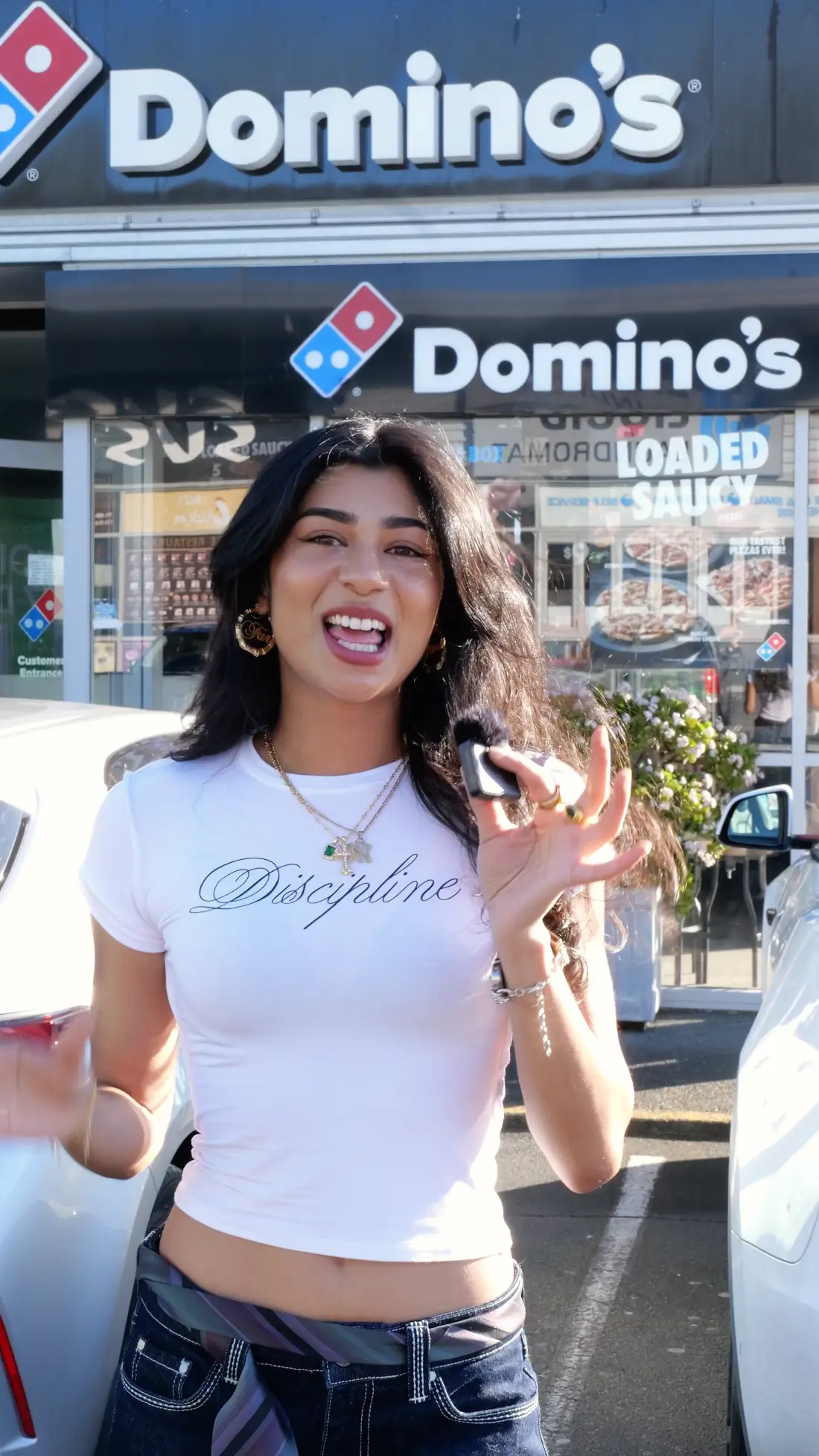 Smiling woman wearing a white shirt with 'Discipline' text standing outside a Domino's Pizza store.