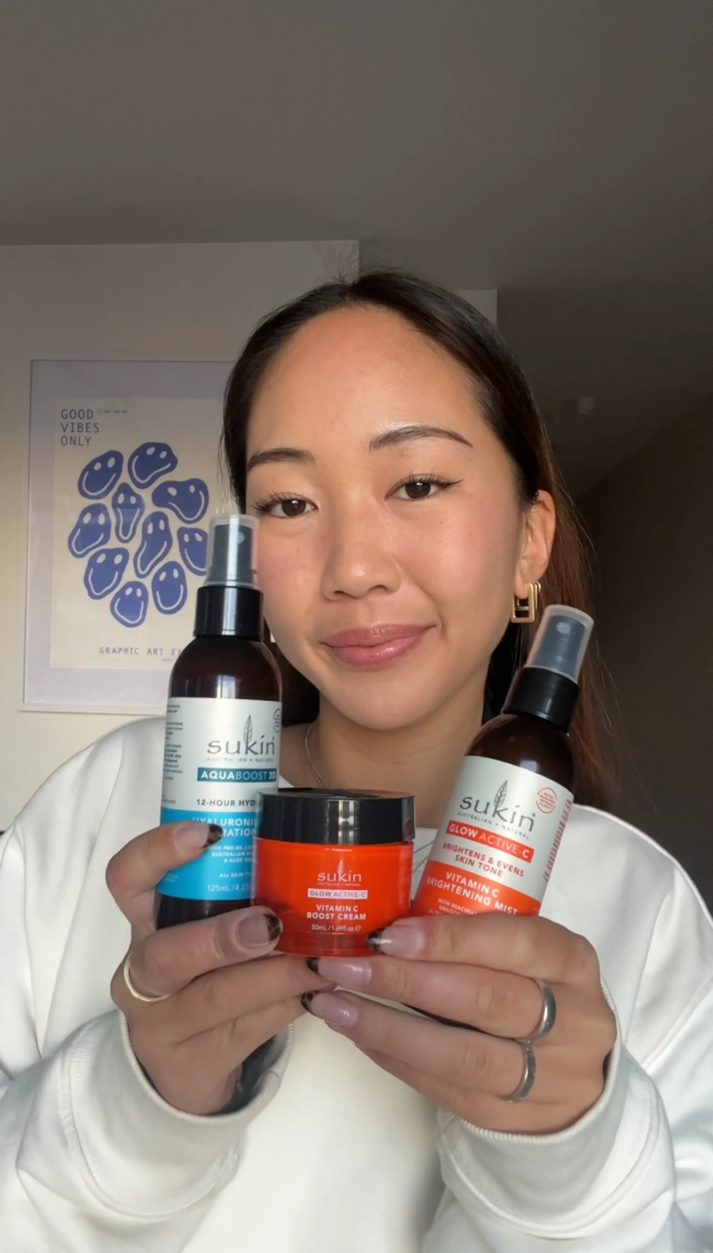 Smiling woman holding three Sukin skincare products including AquaBoost 3D Hydration mist, Vitamin C Boost cream, and Vitamin C Brightening mist.