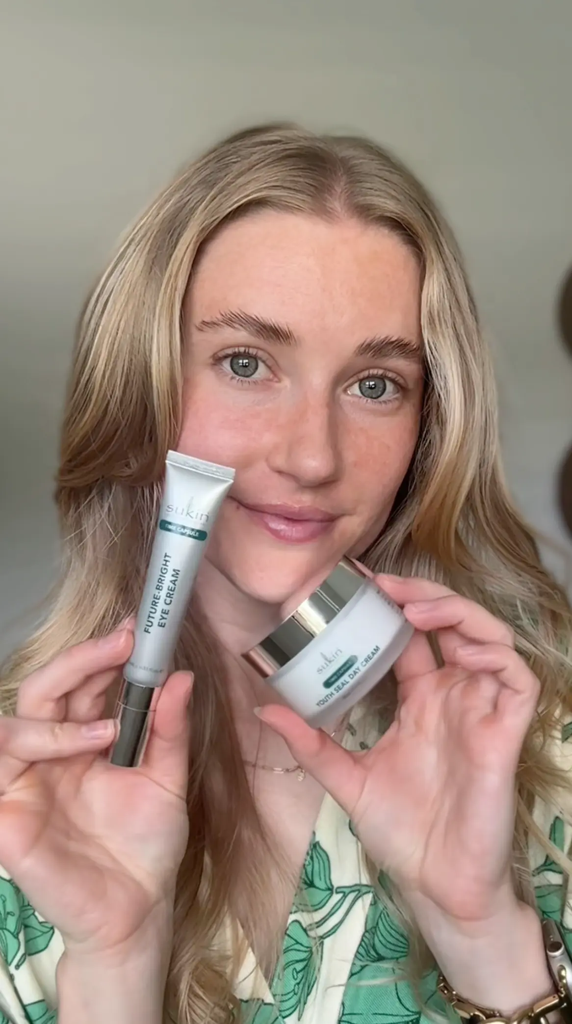 Woman with blonde hair holding Sukin Future Bright Eye Cream tube and Youth Seal Day Cream jar near her face.