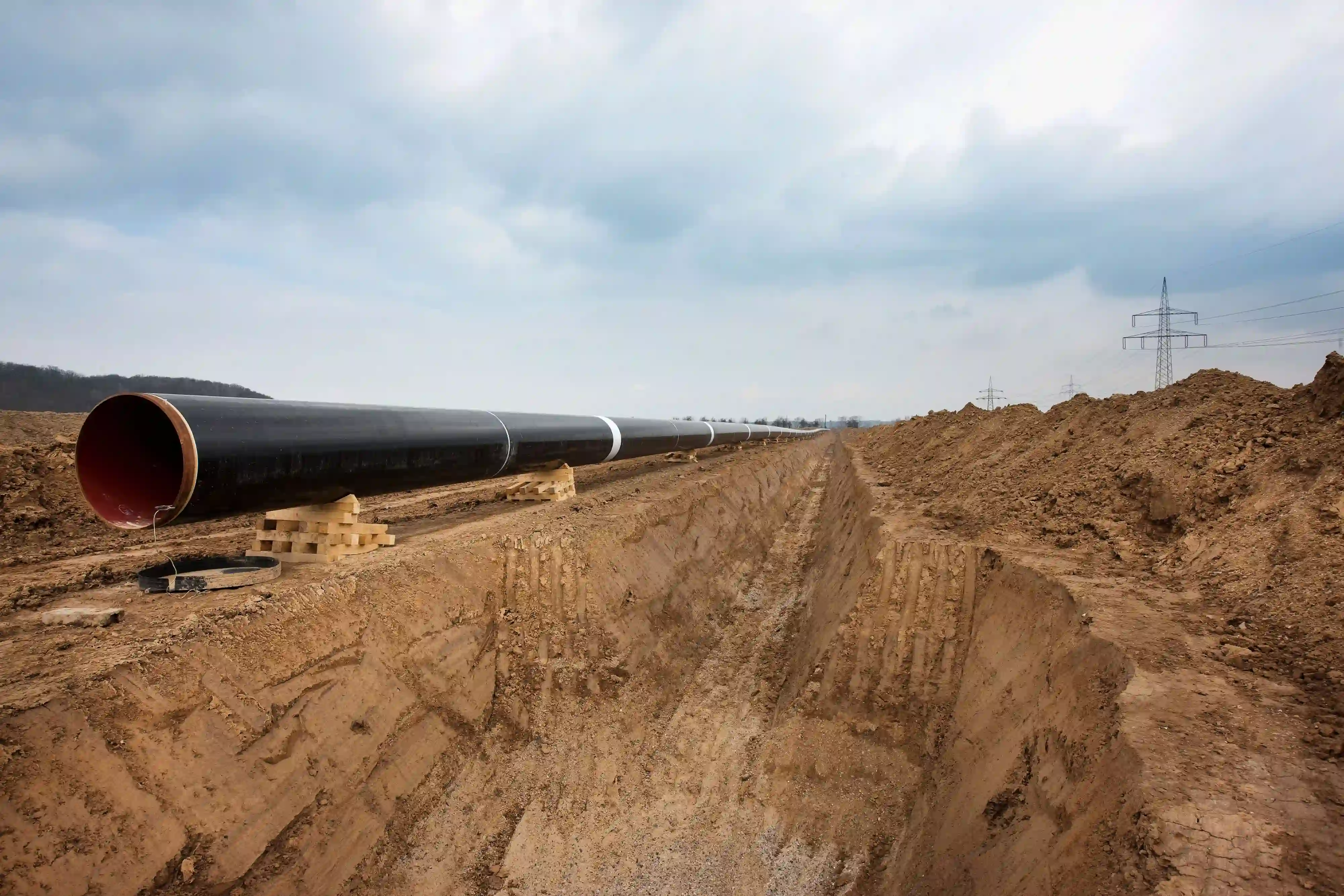 Große schwarze Gasleitung neben einem langen Bodengrabungsgraben unter einem bewölkten Himmel.