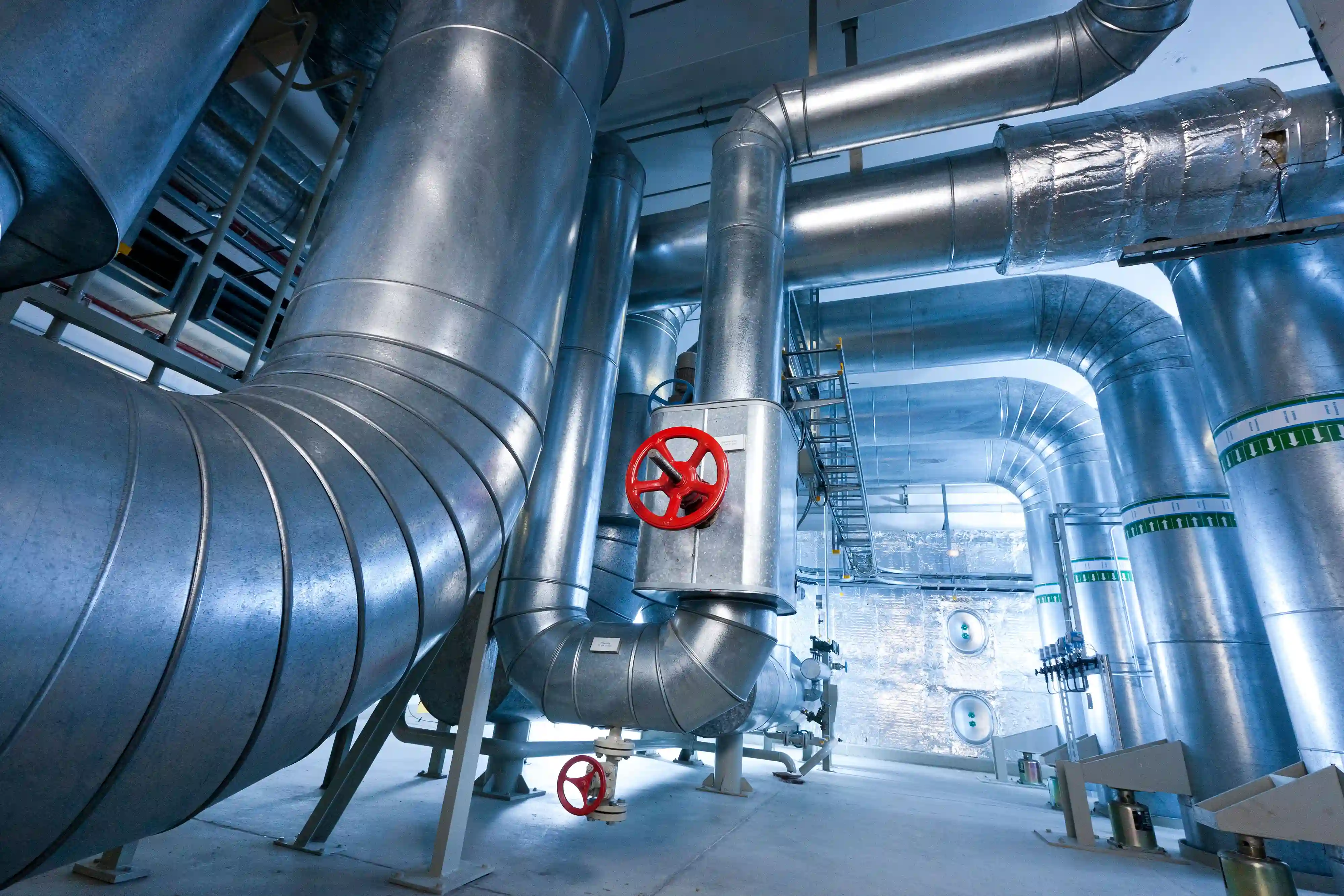 Große industrielle Lüftungs- und Rohrleitungssysteme mit roten Ventilen in einem sauberen technischen Raum.