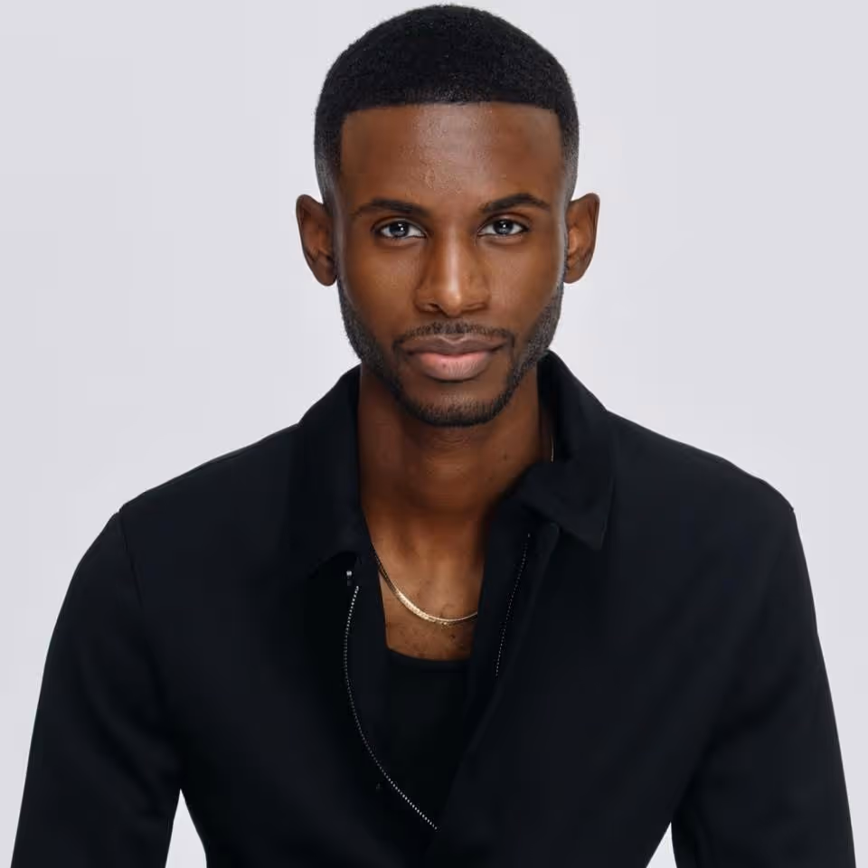Smiling man with shoulder-length curly hair wearing a black t-shirt against a plain white background.