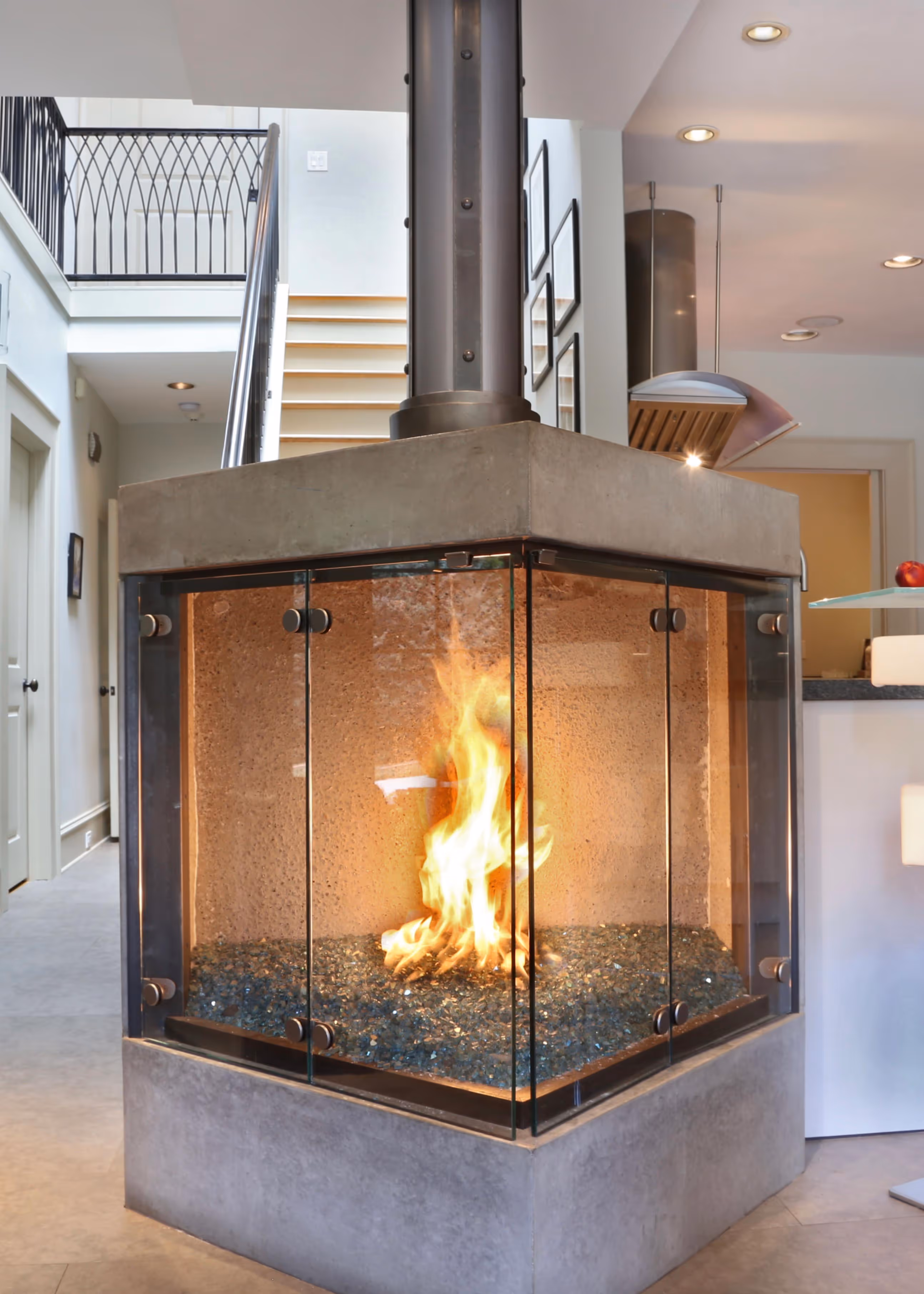 Modern living room with a gray sectional sofa decorated with red and white pillows, glass coffee table with crystal decor, indoor plants, and sunflower bouquet on a side table.