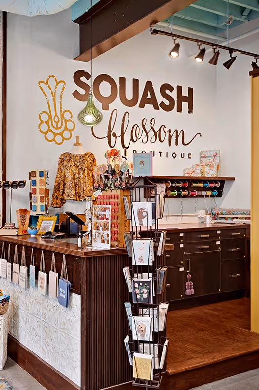 Interior of Squash Blossom Boutique with a display counter, gift cards, craft supplies, and a floral blouse on a mannequin.