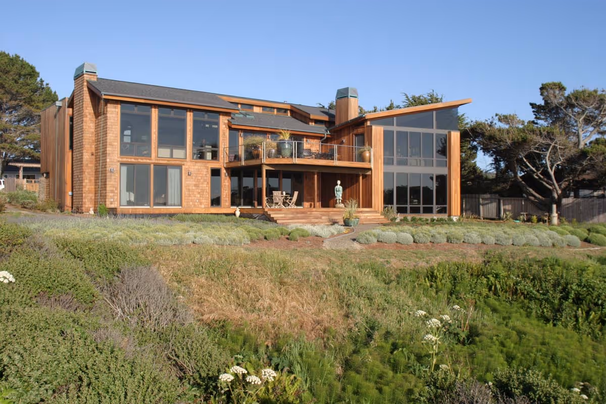 Cozy living room with gray sectional sofa, decorative pillows, glass coffee table with crystal candlesticks, green plants, and sunflowers in a red vase.