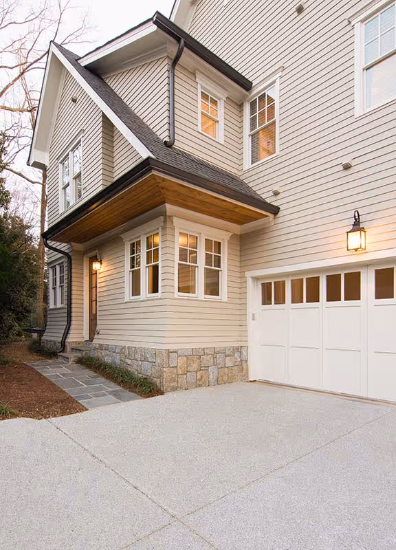 Modern three-story townhouses with garages, trees, and people walking near parked black truck on a sunny day.