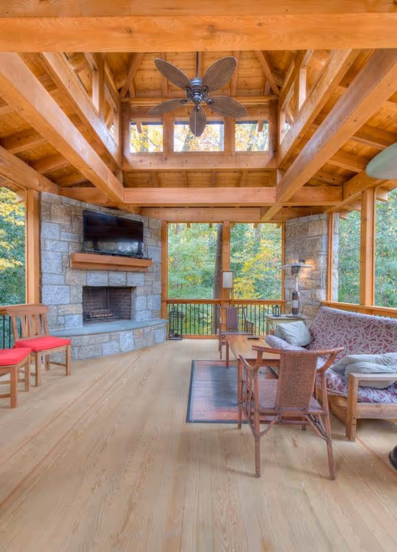 Spacious loft area with wooden floor, brown leather bench, dark wooden bookcase, beige armchair, and large window with greenery outside.