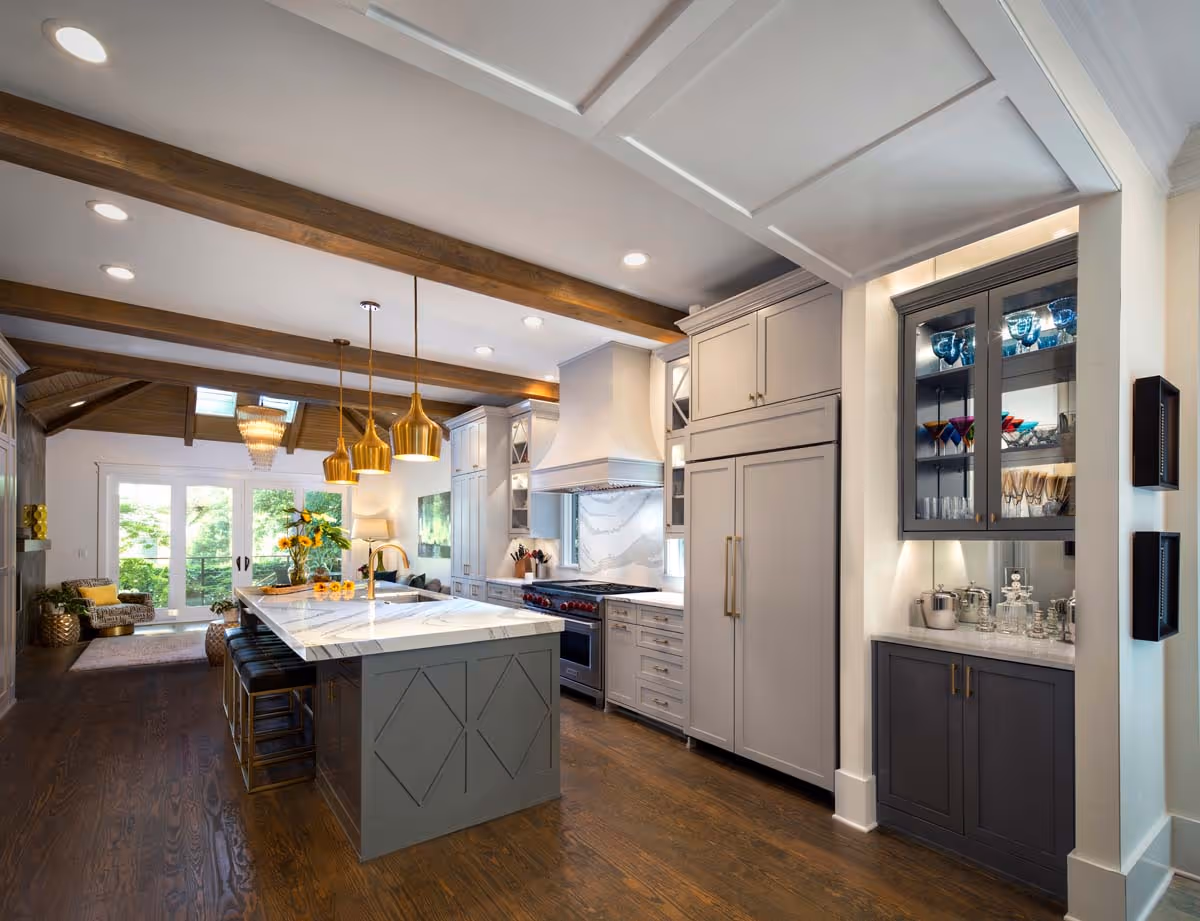 Cozy living room with a gray sectional sofa adorned with red and white patterned pillows, glass-top coffee table with decorative pieces, indoor plants, framed wall art, and a vase of sunflowers on a side table.