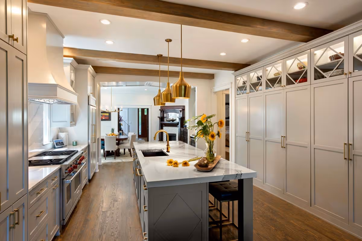 Interior of a boutique with patterned rug, wicker chairs, round table with flowers and skincare products, gold shelves with candles and lotions, framed fashion prints on a red textured wall, and a sculpture on a stand.