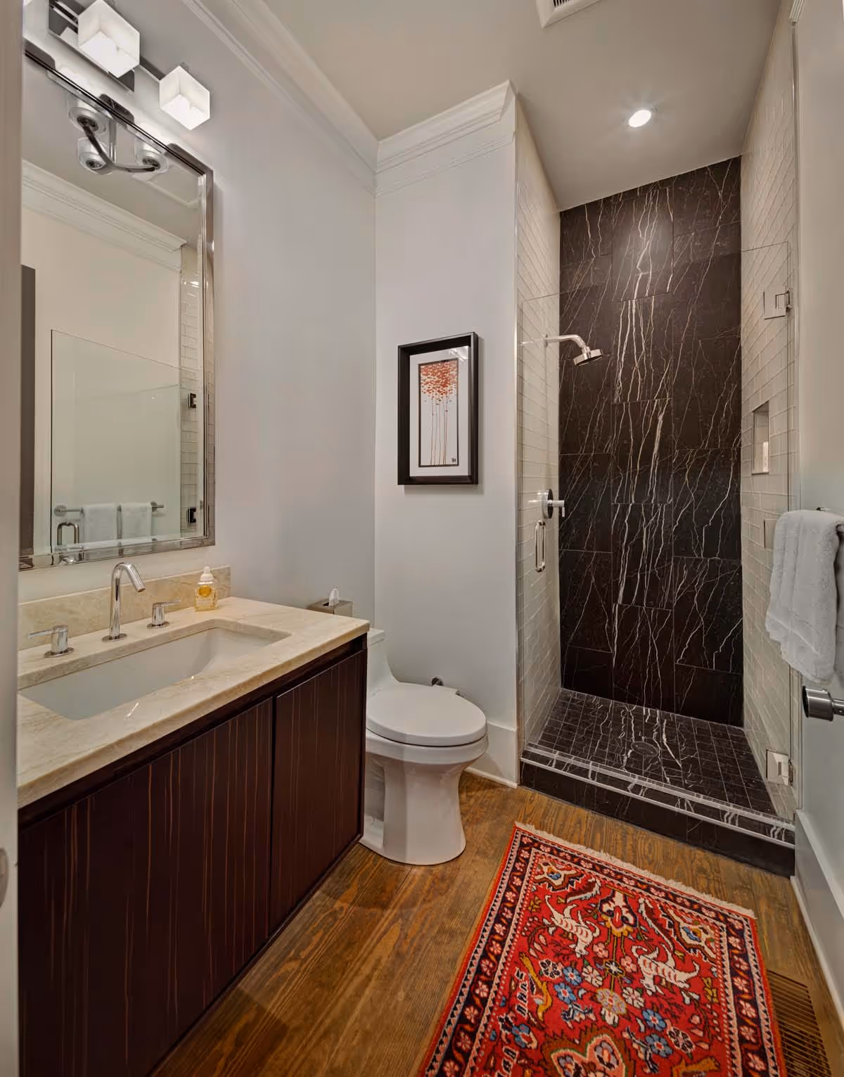 Modern bathroom sink with white basin, red marble countertop, vibrant red flowers in a glass vase, and colorful artwork featuring bandana-wearing figures reflected in a mirror.