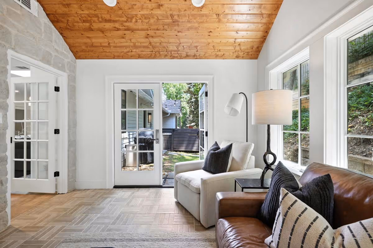 Residential patio with a swimming pool, two lounge chairs with orange cushions, potted plants, and outdoor seating under a covered porch.