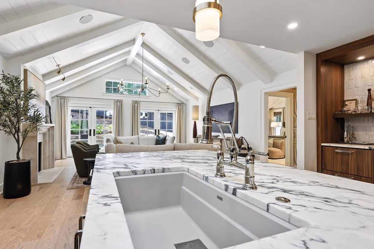 Bright living room with large windows, a grand piano, gray armchair, light gray sofa, colorful flowers, and built-in white bookshelves.