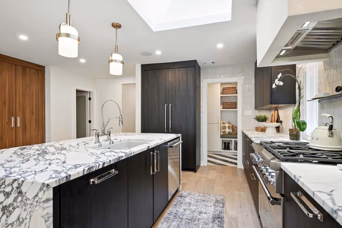 Modern bathroom with double sinks, large mirrors, a potted plant on the counter, and a walk-in closet visible through an open door.