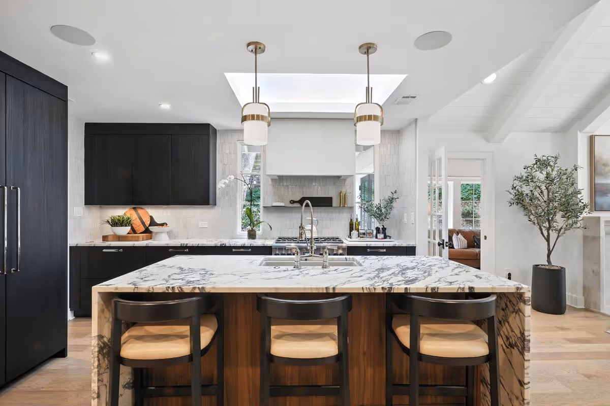 Bright attic living space with a brown leather bench, dark wooden cabinet filled with books, cozy seating area, green plants, and railing overlooking lower floor.