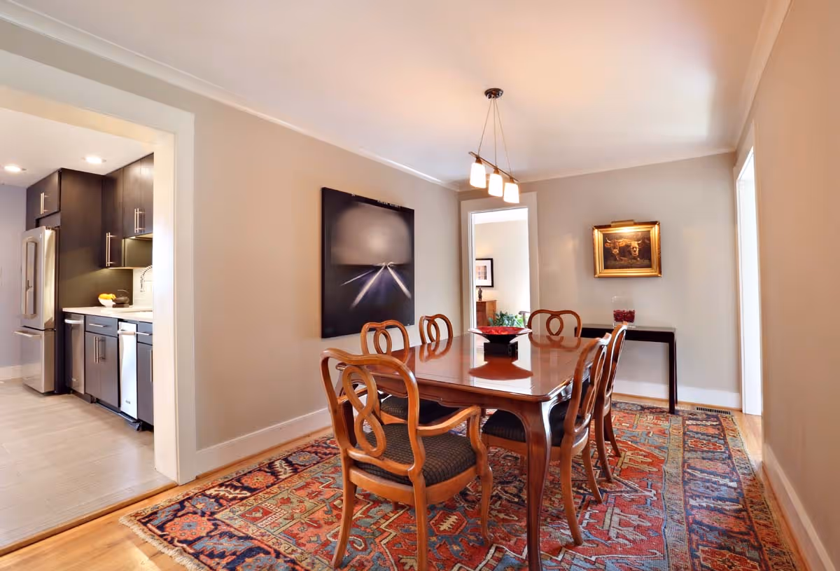 Modern living room with a white armchair, brown leather sofa, potted plant by the fireplace, and large windows.