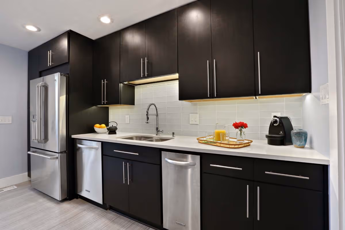 Two-story beige and brown residential buildings with balconies surrounded by green lawns and autumn-colored trees under a partly cloudy sky.