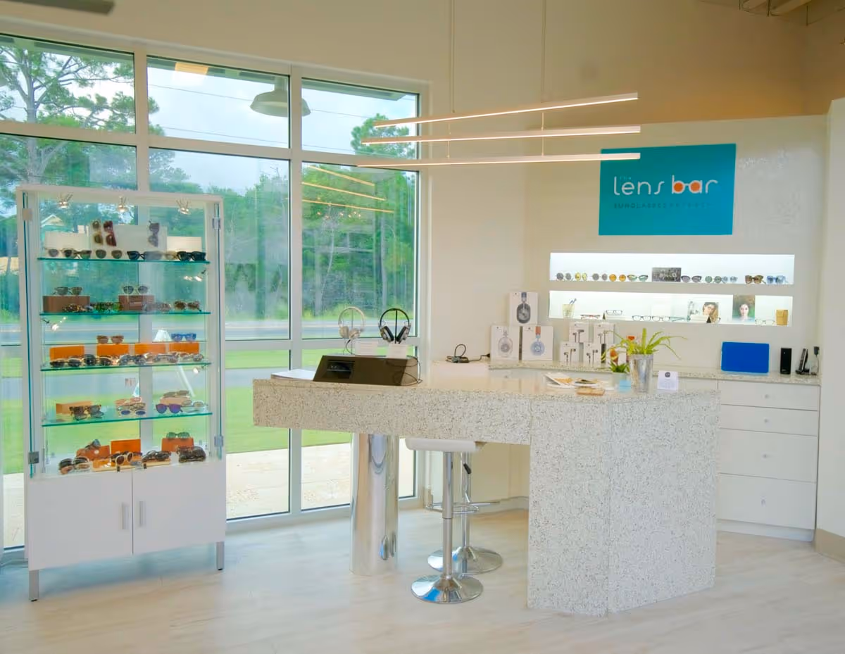 Modern bathroom sink with a white vessel basin mounted on a brown marble countertop, a wall-mounted faucet, a vase of red and orange flowers, and a colorful framed painting of three people wearing bandanas.