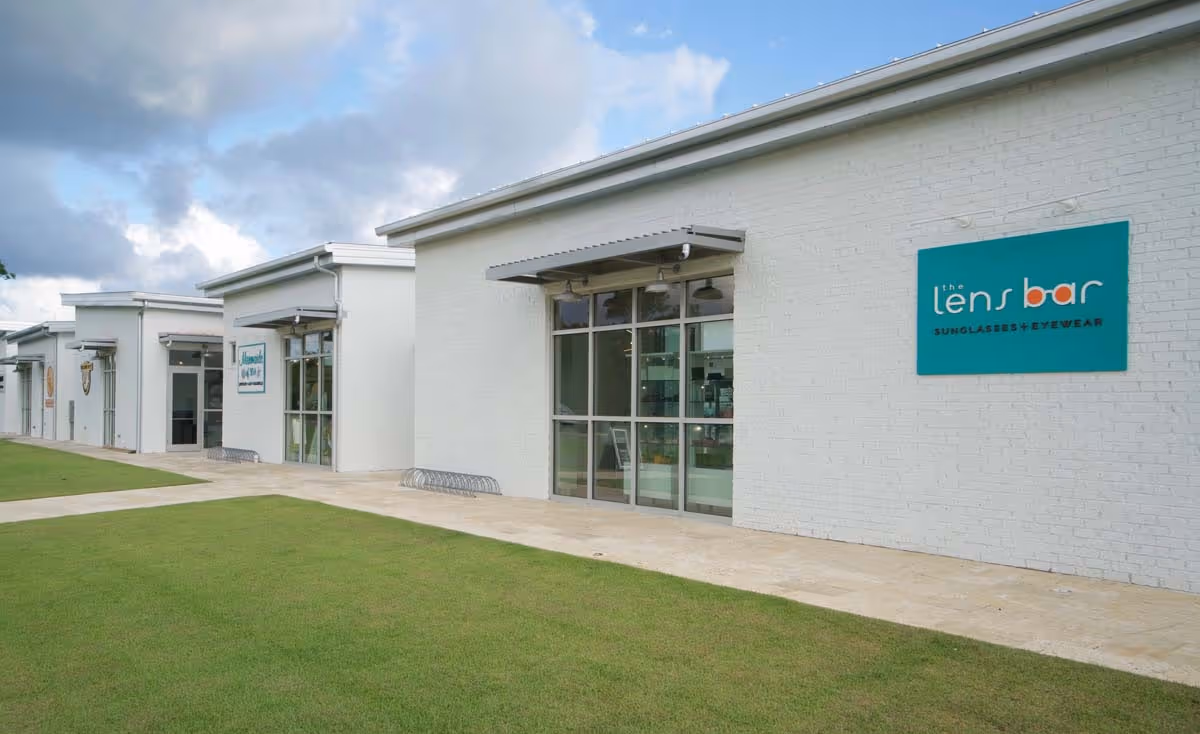 Sunlit porch with two metal mesh chairs, stone half-wall, and metal railing overlooking green trees and bushes.