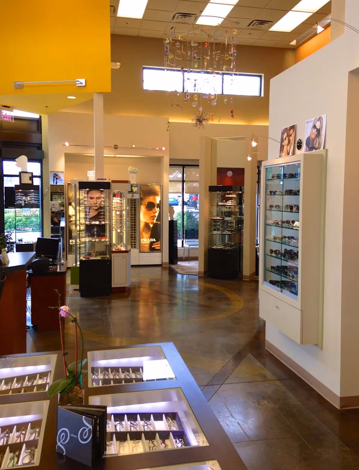 Modern optical store interior with eyeglass displays, brand posters, and a chandelier hanging from the ceiling.