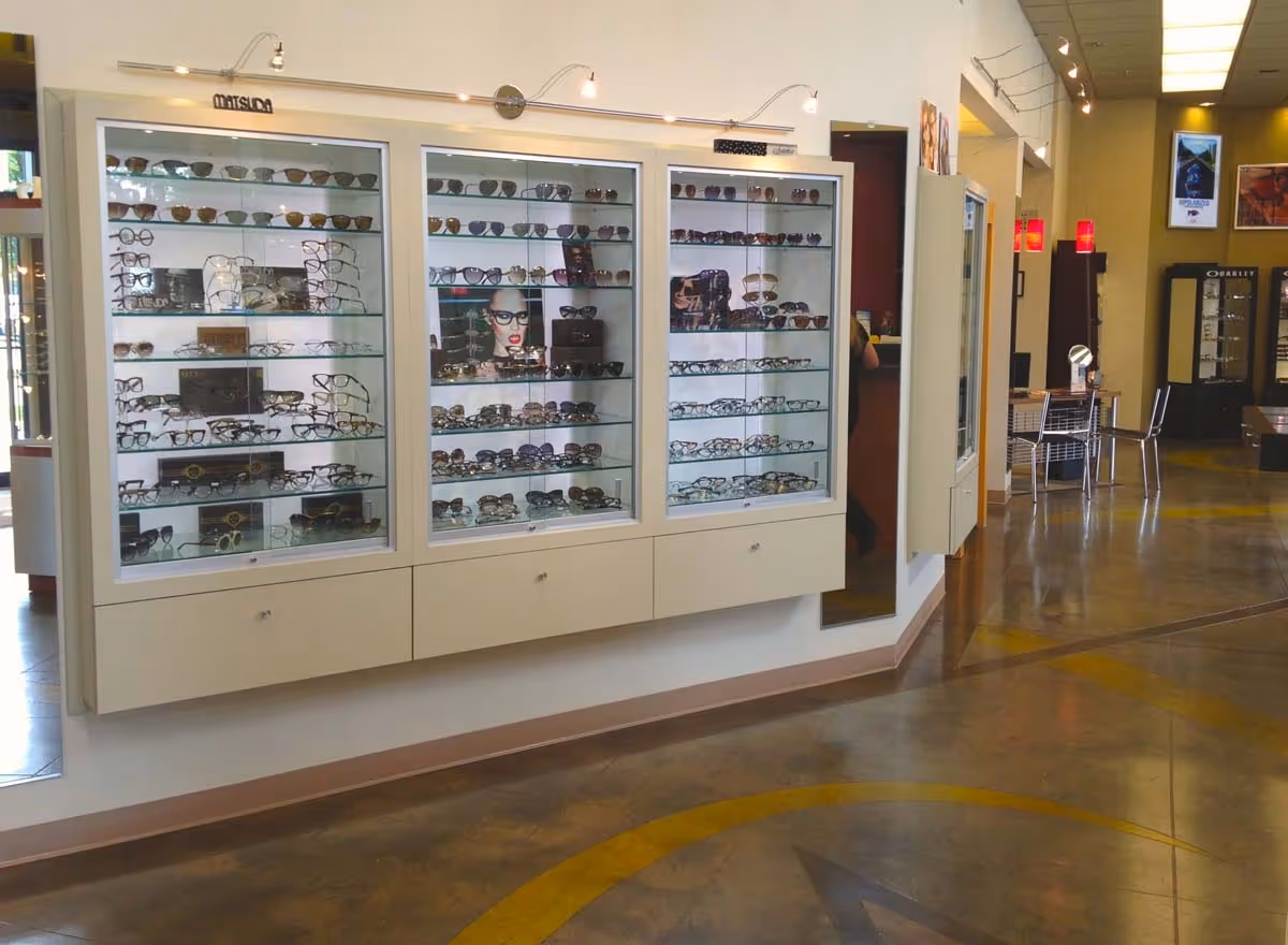 Interior of an eyewear store displaying various sunglasses and eyeglasses in three glass cabinets with illuminated shelves.