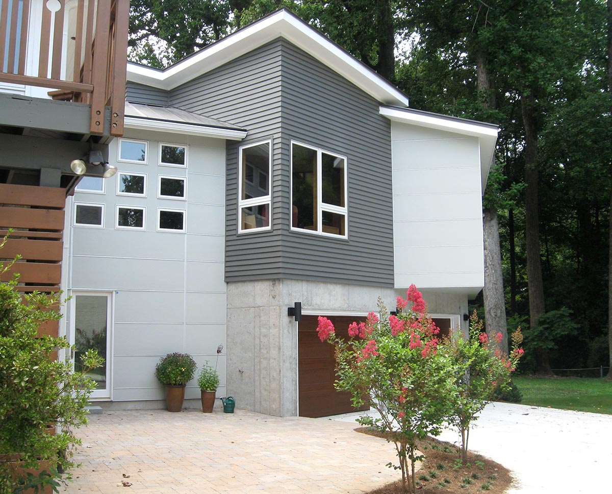 Sunny porch with two metal mesh chairs, stone half-wall, metal railing, and green trees in the background.