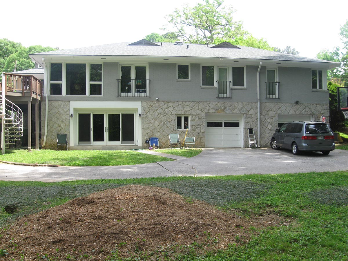 Sunny porch with two metal mesh chairs, stone half-wall, metal railing, and green trees in the background.