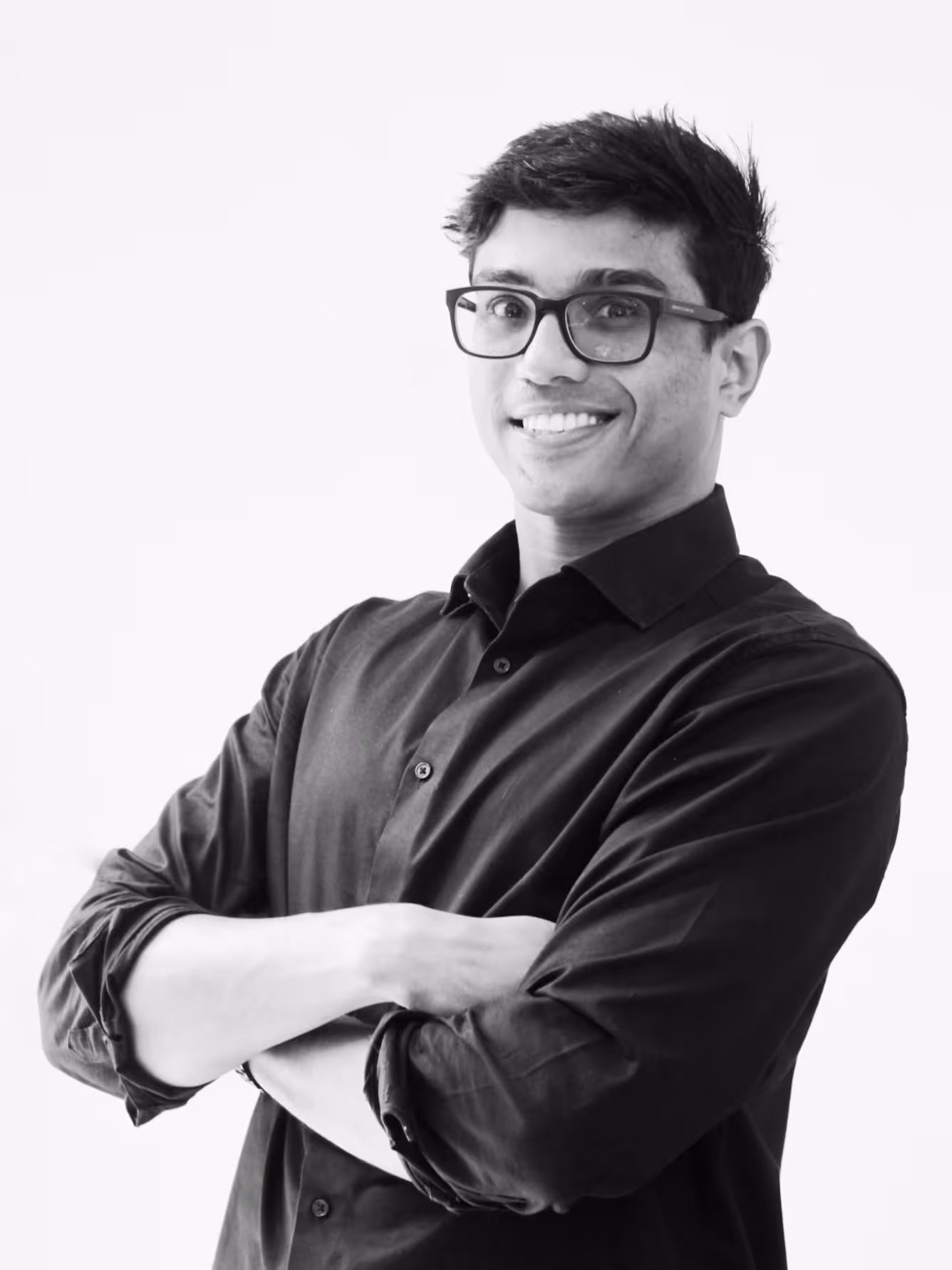 Young man with glasses and a goatee smiling in front of a bookshelf filled with books.