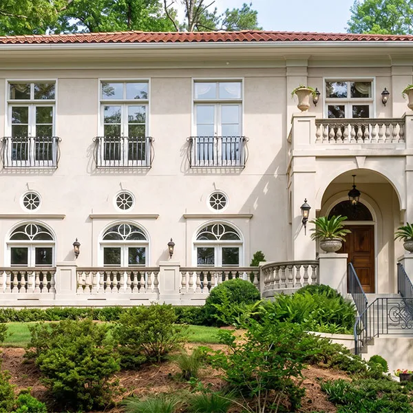 Modern two-story house with large windows, surrounded by green trees and lawn under an overhanging tree canopy.